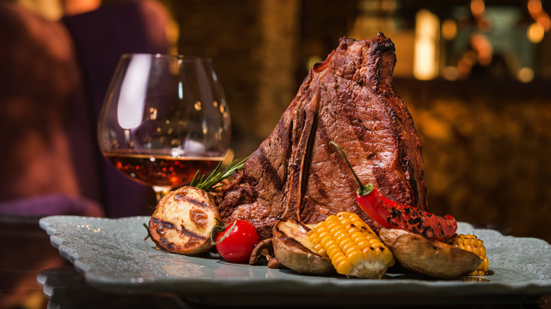 A glass of whiskey next to a plate of grilled steak and vegetables