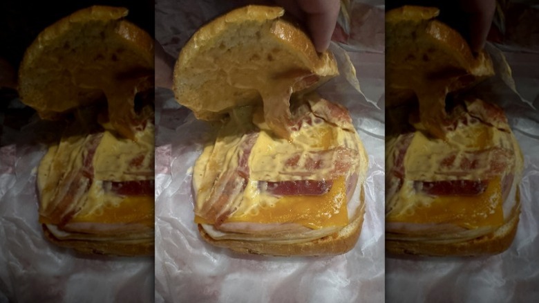 A person holding up the top bun of Buc-ee's Club Melt to show off its contents.