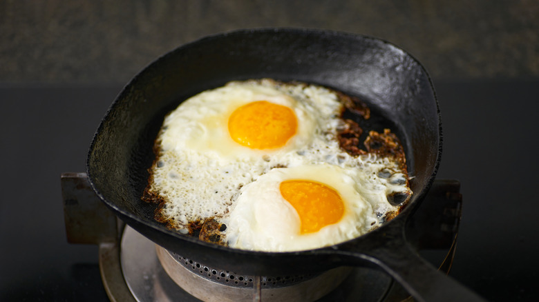 two fried eggs with burned edges cooking in a cast iron pan