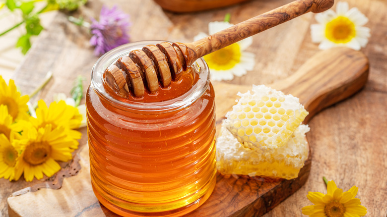 honey stick sitting in jar of honey in kitchen with flowers