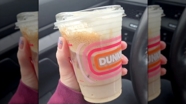 A woman holding a Dunkin' Dirty Soda in her car.