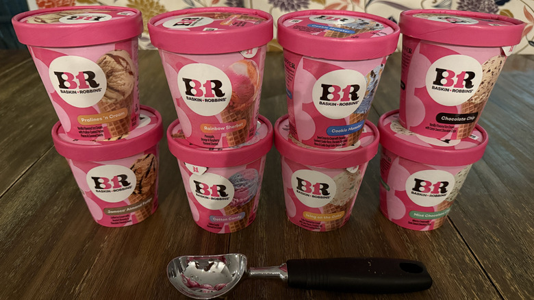 Eight flavors of Baskin Robbins ice cream on a wooden table with ice cream scooper