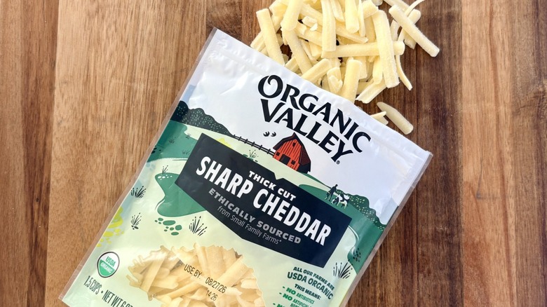 An open bag of Organic Valley thick cut sharp cheddar cheese on a cutting board