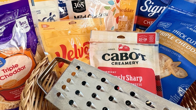 A group of different shredded cheese brands alongside a box grater