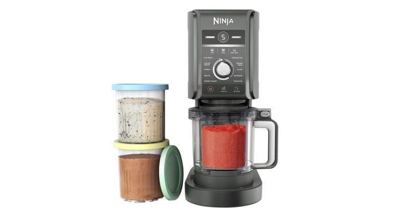 The Ninja CREAMi Deluxe 11-in-1 Ice Cream and Frozen Treat Maker with two jars of ice cream beside it and one within it.
