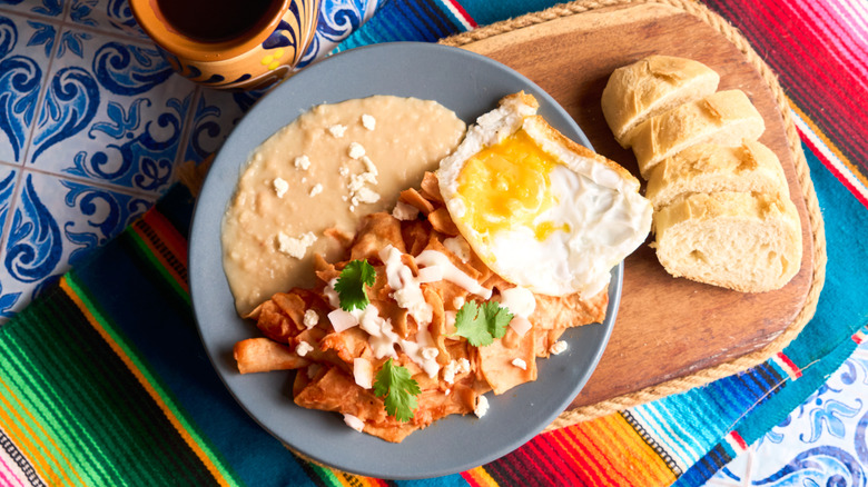 Top view of Mexican breakfast with chilaquiles, refried beans, fried egg, sliced bread, and coffee
