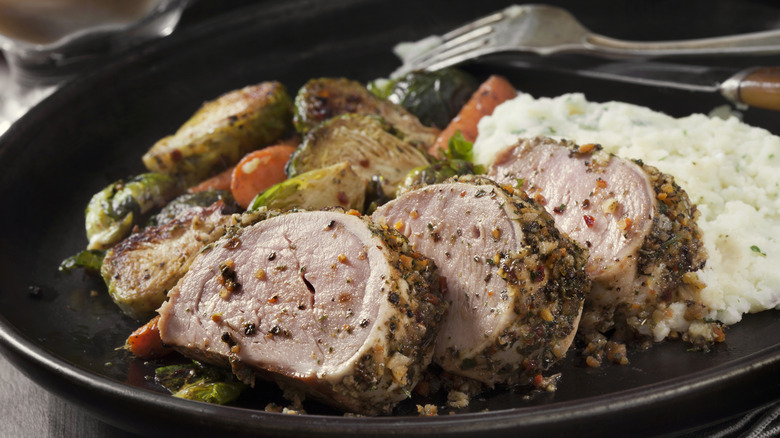 Sliced pork roast on plate with vegetables and mashed potatoes