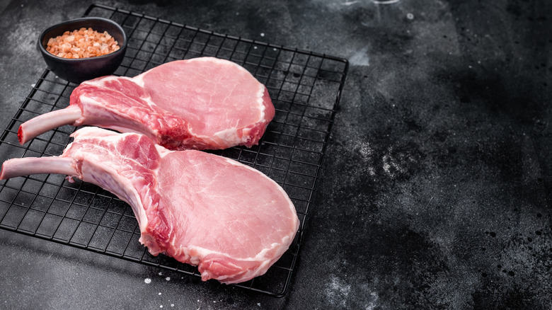 Two raw pork chops with salt on a cooking rack