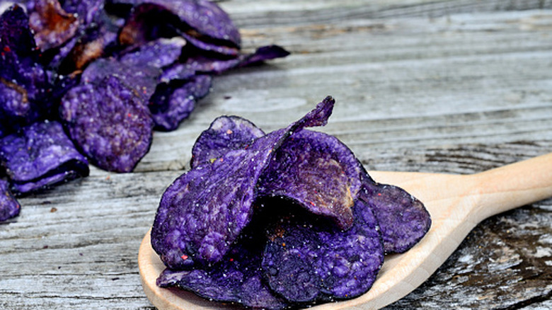 Blue potato chips in a wooden spoon on wooden table