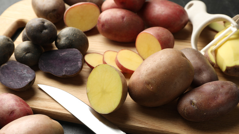 Different types of potatoes with a peeler and knife on a wooden chopping board