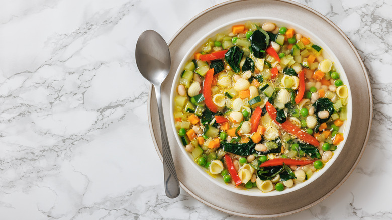 Minestrone soup with spoon on marble backdrop