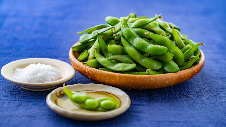 Edamame pods and salt on small plates on blue tablecloth