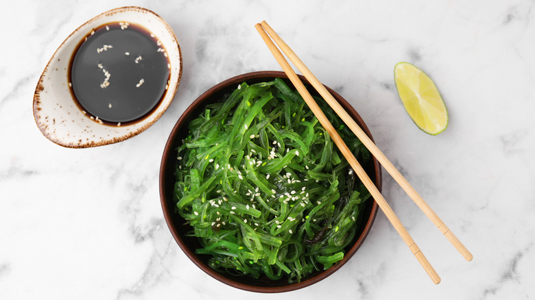 Seaweed salad with chopsticks by soy sauce ramekin and lime wedge