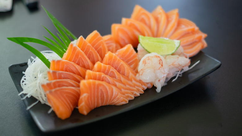 Salmon and shrimp sashimi with radish garnish on black serving plate