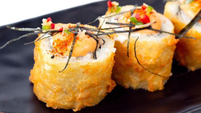 Fried sushi roll topped with nori strips on black plate