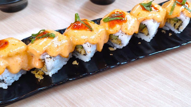 Dynamite sushi roll loaded with spicy mayo on black plate
