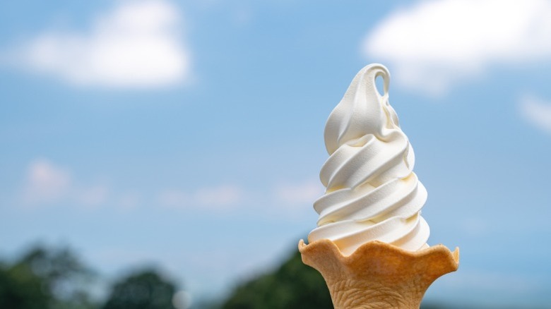 A cone of soft-serve ice cream with trees and blue sky in the background