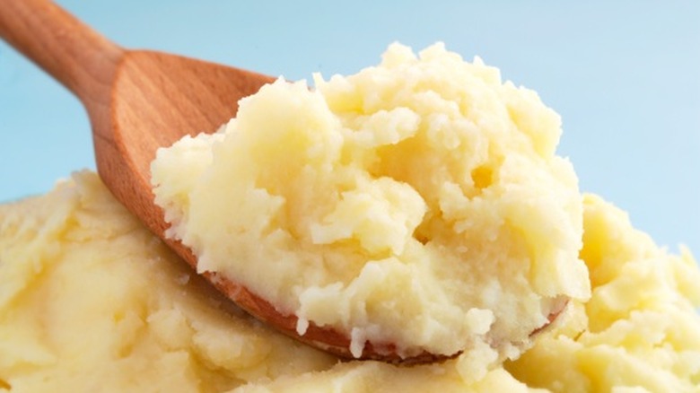 An up-close shot of mashed potatoes in a spoon over a bowl