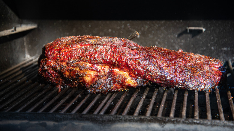 A close-up shot of a brisket cooking on a barbeque grill, topped with a sauce