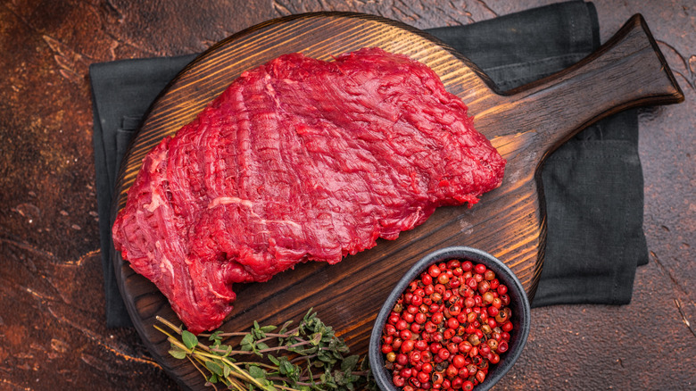 Flank or Flap steak, raw beef meat with thyme on wooden board. brown background. top view.