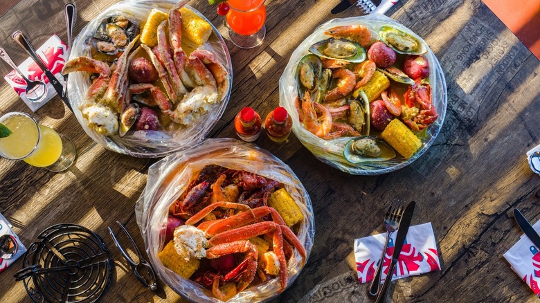 A bunch of seafood boil on a table with corn, lemons, shrimp, and potatoes in three different silver metal bowls.