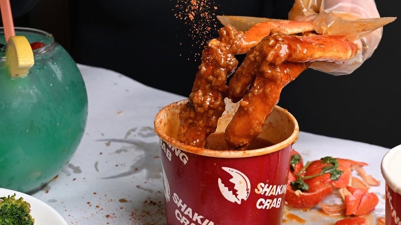 A person sprinkling seaoning onto a king crab claw dipping into a sauce.