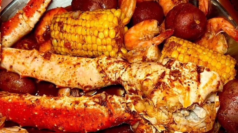 Crab legs, shrimp, potato, and corn on the cob in a dish together.
