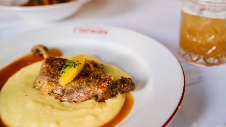 Duck à l'orange on white plate with cocktail nearby
