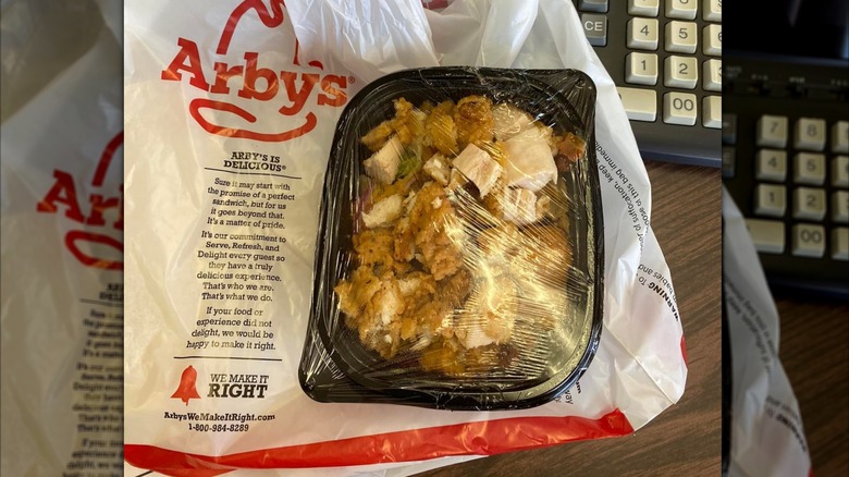 An Arby's crispy chicken salad sits on Arby's bag on a desk