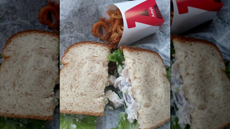Arby's Pecan Chicken Salad Sandwich cut in half under curly fries on white paper