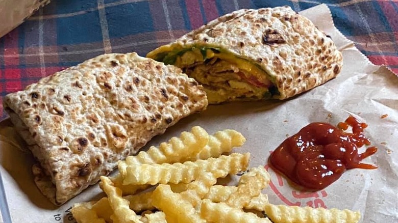 A chicken club wrap with fries and ketchup sits on a plaid surface