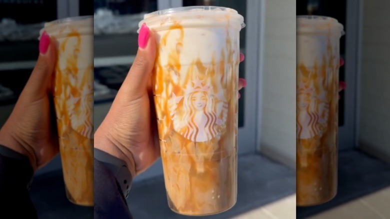 A hand holding up the Iced Banana Bread Latte from Starbucks in front of the store.