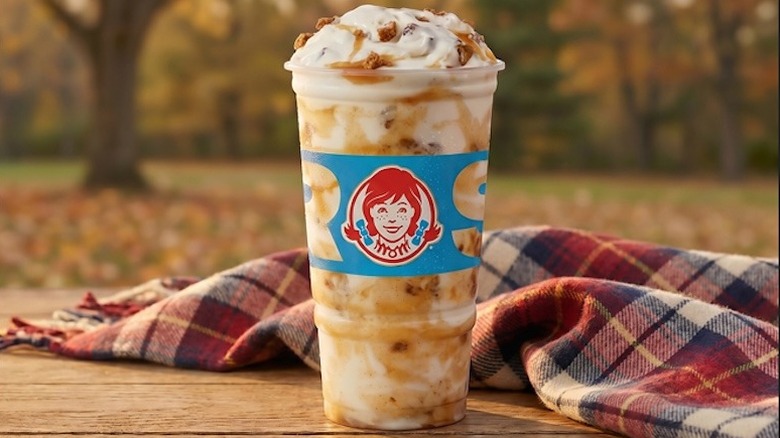A product image of Wendy's Apple Crumble Frosty Fusion with an outdoor fall scene in the background.