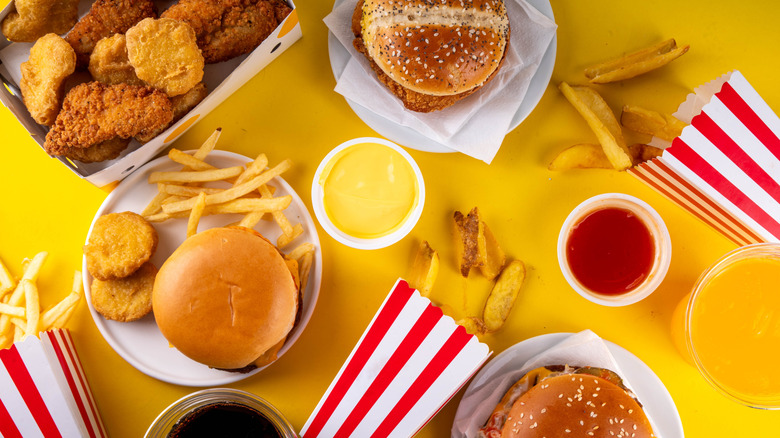 Top view of assorted fast food dishes including burgers, chicken nuggets, and fries on yellow background