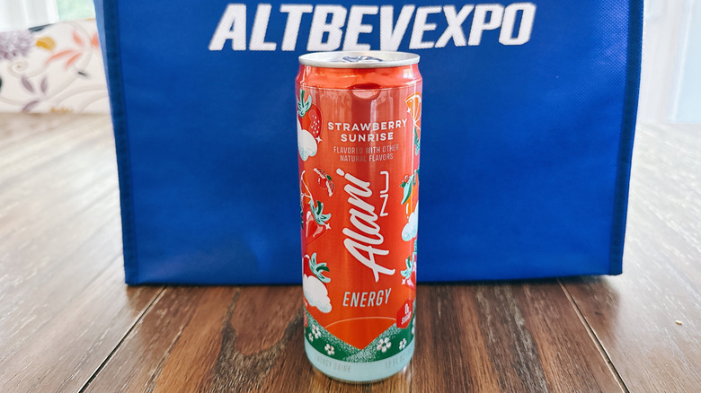 Alani Nu can on wooden table in front of a blue bag from the Alt Bev Expo