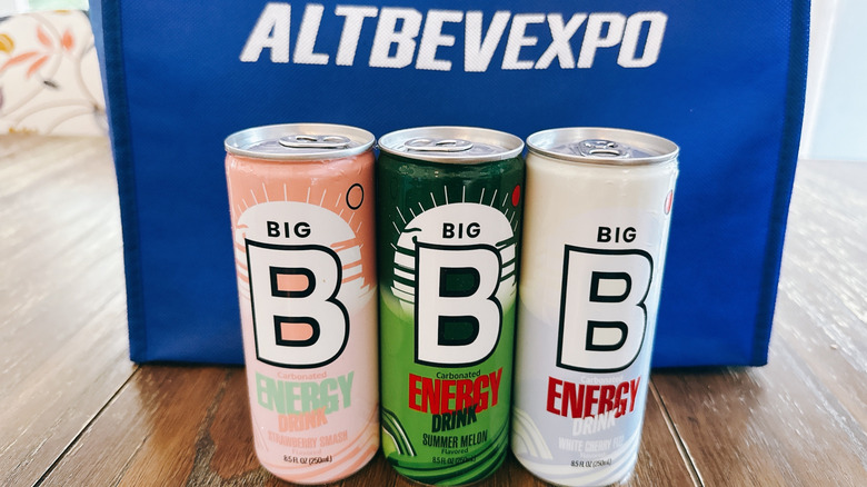 Big B Energy cans on wooden table in front of a blue bag from the Alt Bev Expo