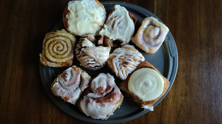 Nine grocery store bakery cinnamon rolls on a tray on a wooden surface.