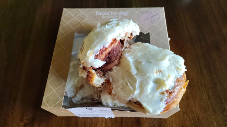 Two messily frosted Favorite Day Bakery cinnamon rolls sit atop a bakery box.