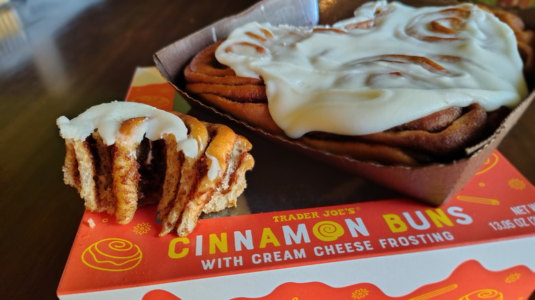 Half of a Trader Joe's Cinnamon Bun placed next to a tray of the frosted buns, with the packing underneath both.
