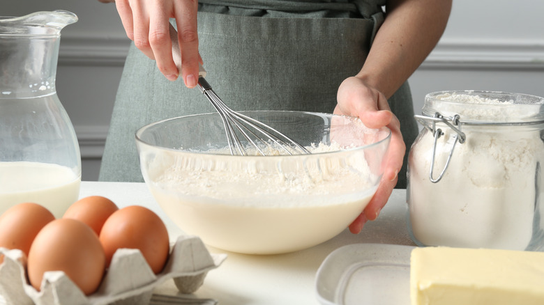 Woman making batter (liquid dough) at white table indoors, closeup