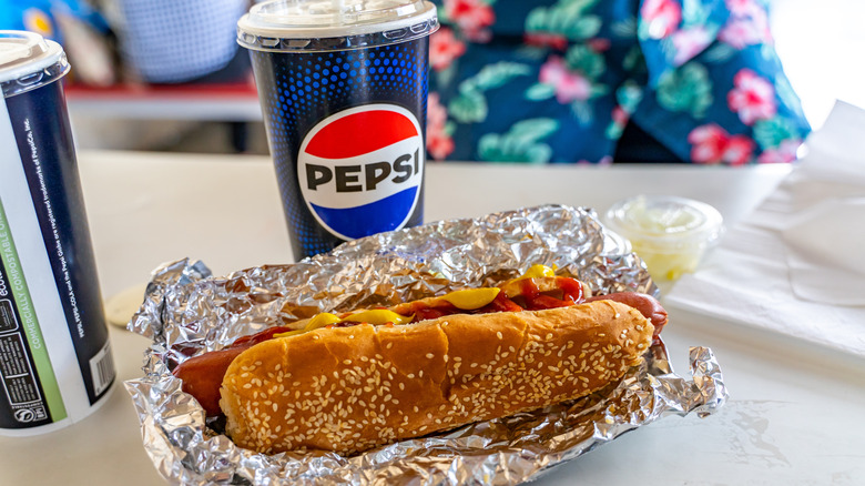 A Costco hot dog beside a 20-ounce Pepsi cup, both of which are included in the $1.50 Hot Dog Combo