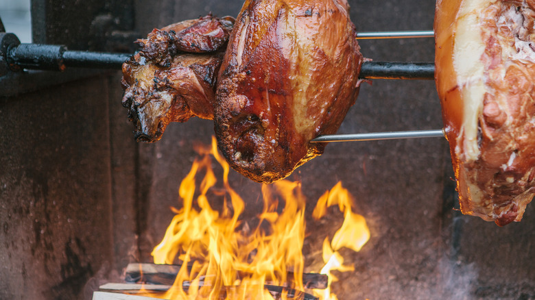 Pork hams slow cooking on rods over an open fire.