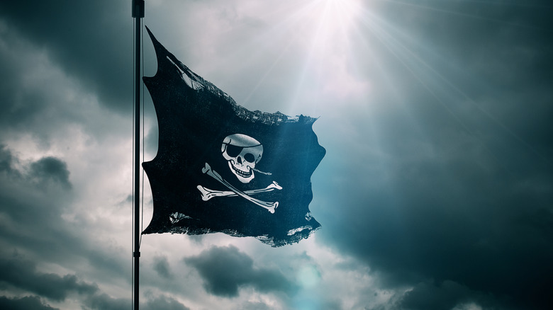 A black flag waves in the wind with a skull and cross bones on it.