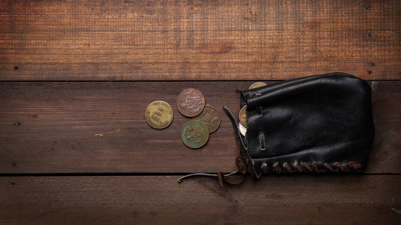 Several coins spill from a leather coin pouch on a rustic wooden table.