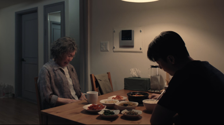 Hwang Jun ho and his mother sit across from each other at a table filled with sides and noodles