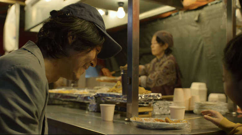 Gi-hun and his daughter smile as they share tteokbokki at a street stand