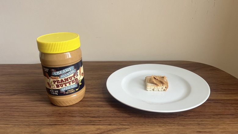 Jar of creamy no stir Trader Joe's peanut butter and some spread on a piece of bread on a round white plate