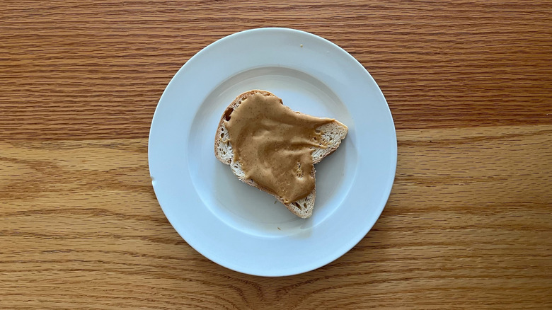 A piece of white bread smeared with peanut butter on a round white plate