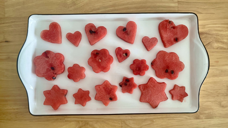 Cookie cutter carved watermelon slices on white tray on wooden table
