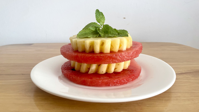 Watermelon stacks with pineapple layer and fresh mint topping on white plate
